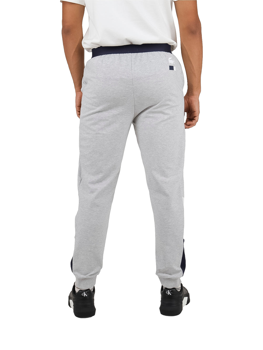 Hombre vistiendo pantalón de pijama gris de Lacoste con cintura elástica azul marino.