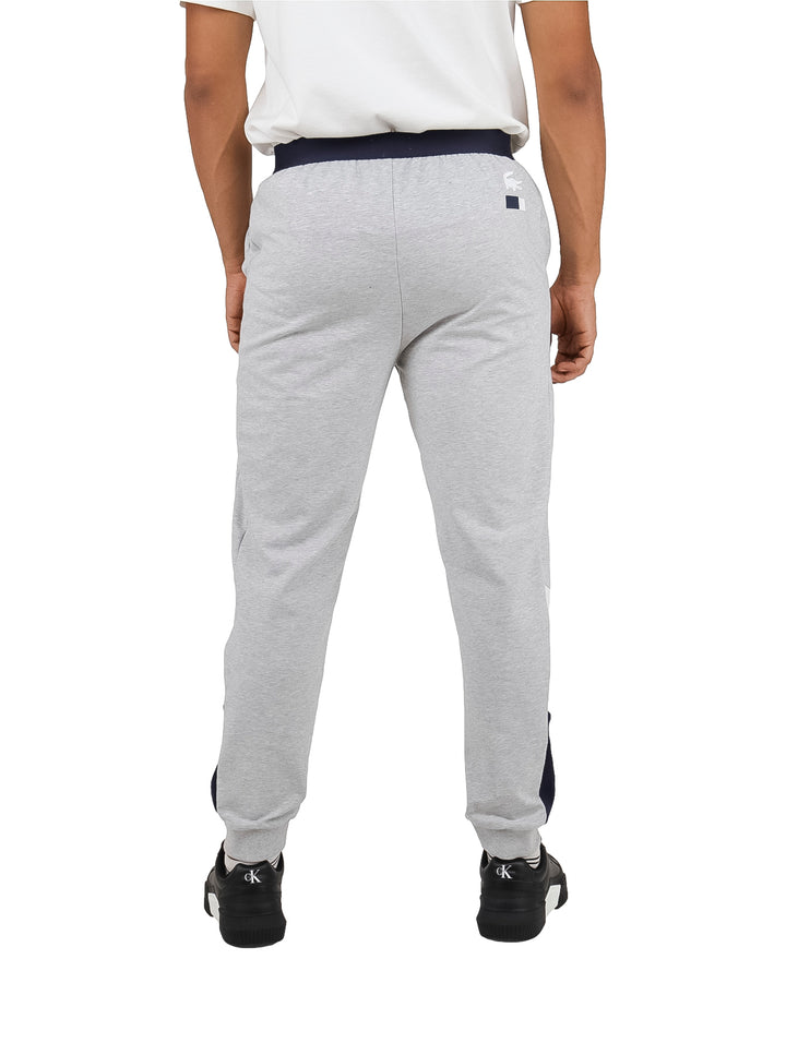 Hombre vistiendo pantalón de pijama gris de Lacoste con cintura elástica azul marino.
