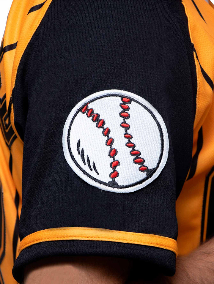 Detalle de la manga de un jersey de béisbol color negro y naranja con un parche de pelota blanca.