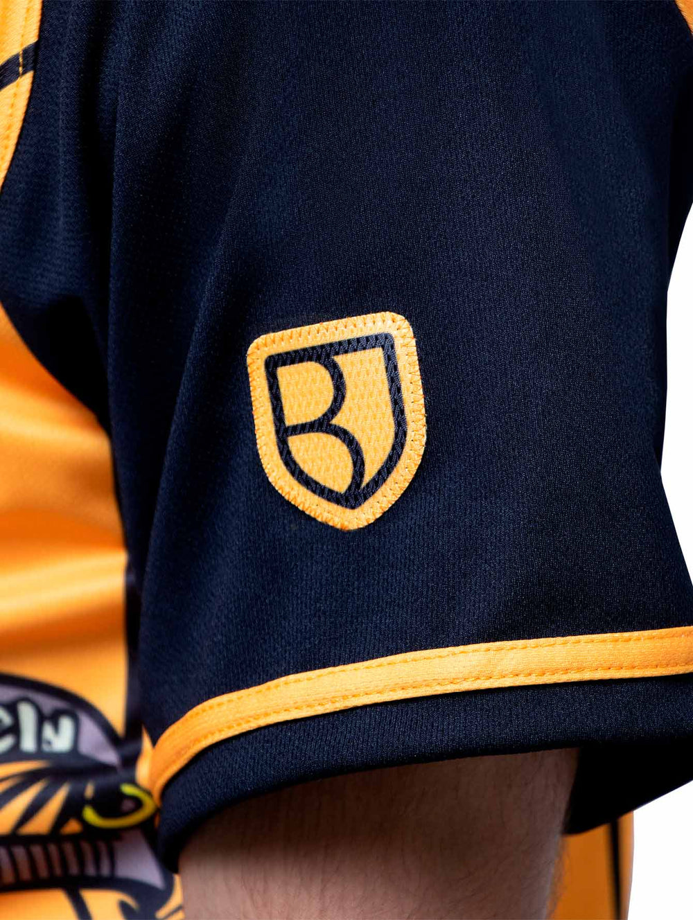 Detalle de la manga de un jersey de béisbol color negro y naranja con un parche de pelota blanca.