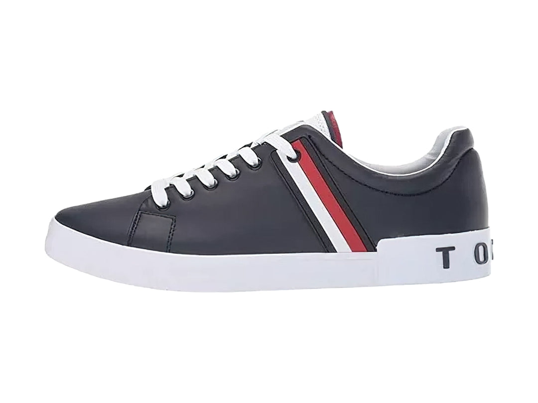 Tenis Tommy Hilfiger color negro con suela blanca y detalle de franja roja y blanca lateral.