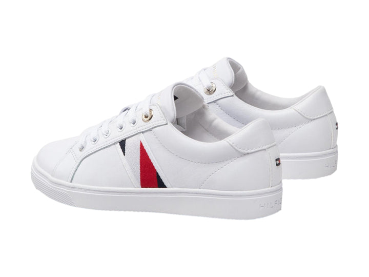 Tenis blancos Tommy Hilfiger de corte bajo con franja lateral en rojo y azul y suela blanca.