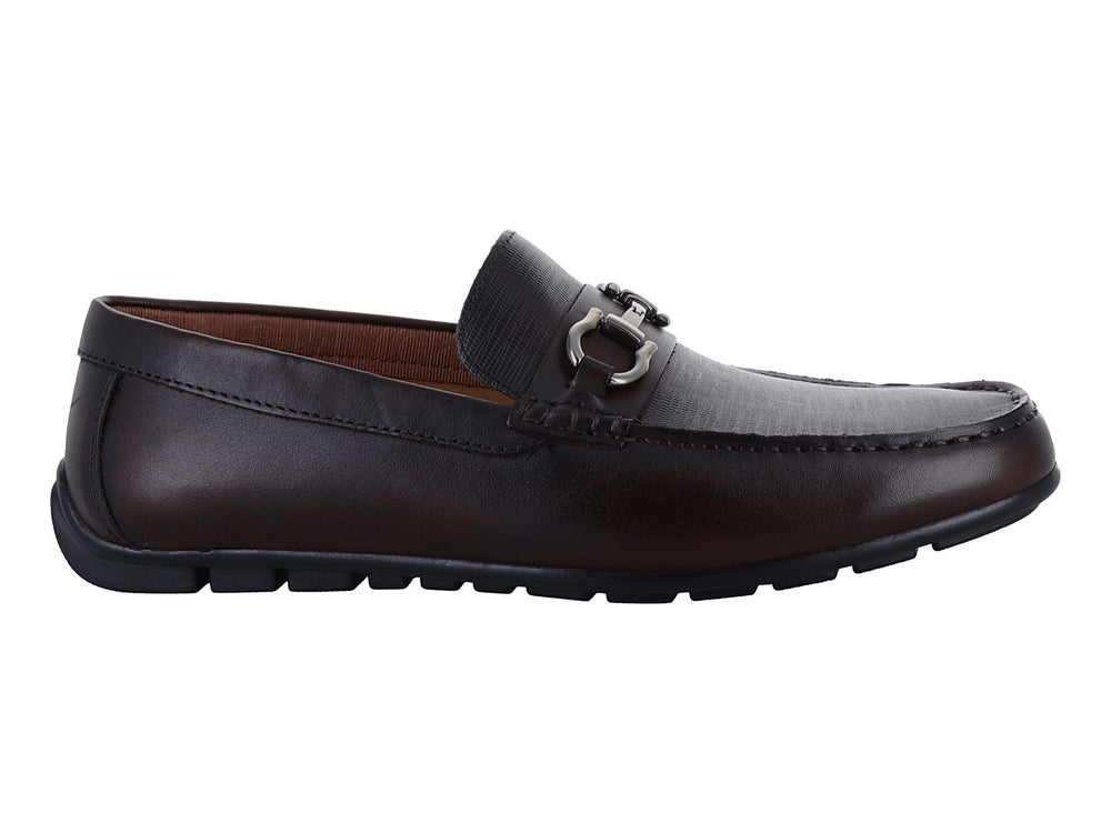 Zapato mocasín de cuero marrón con detalle de herraje metálico plateado en la parte superior.