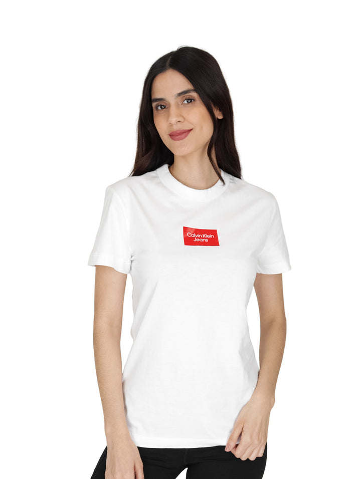 Mujer vistiendo una playera blanca de manga corta y cuello redondo con un logo rectangular rojo en el pecho.