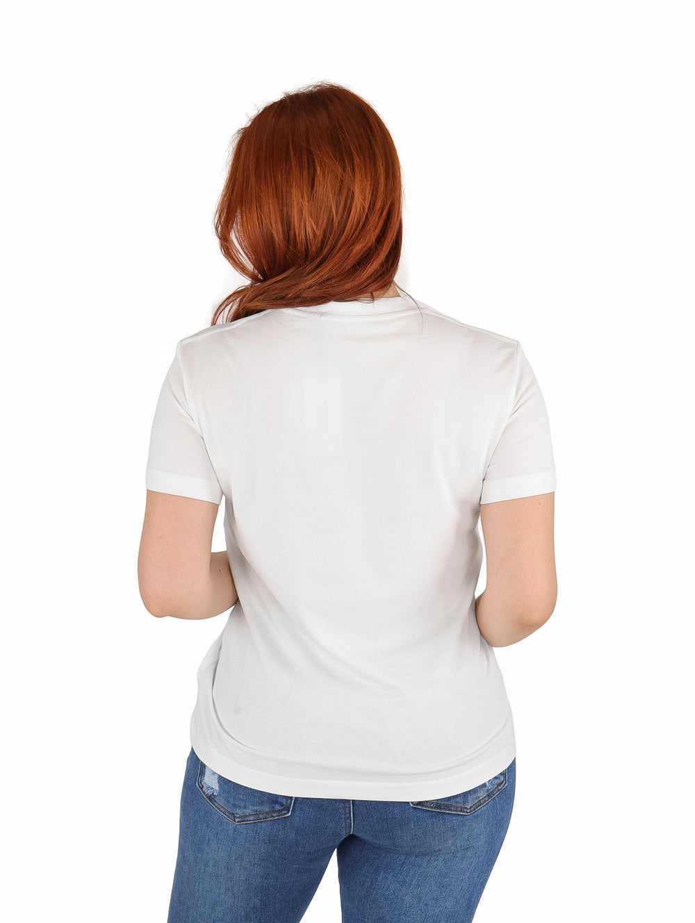 Mujer vistiendo playera blanca de manga corta con estampado central de Calvin Klein Jeans y jeans azules.