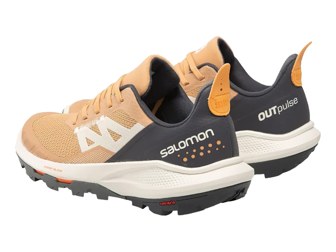 Tenis deportivos Salomon Outpulse en colores beige, gris oscuro y detalles naranjas con suela blanca y negra.