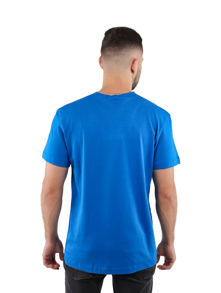 Hombre vistiendo una camiseta azul de manga corta con un pequeño detalle rectangular blanco en el pecho.