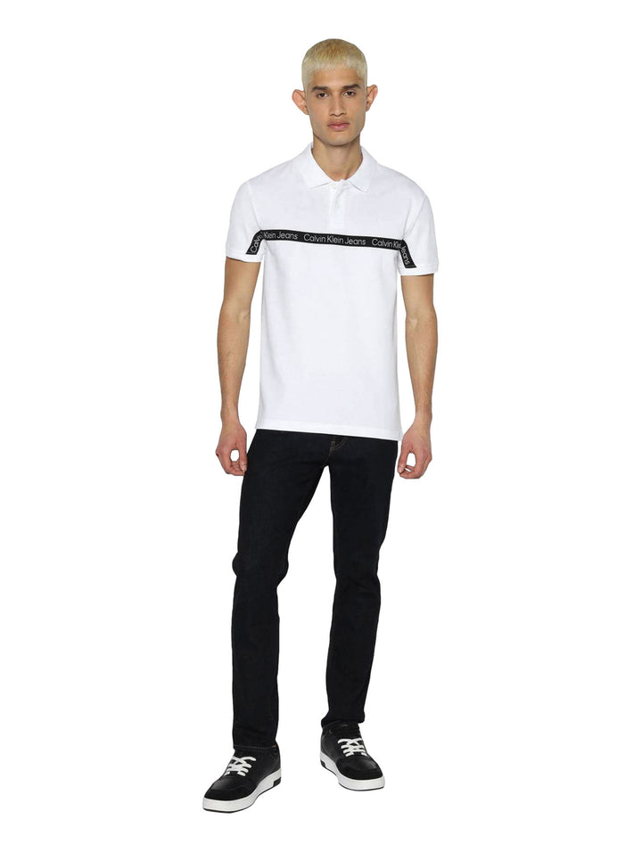Hombre vistiendo polo blanco de Calvin Klein con cinta negra con logo en el pecho.