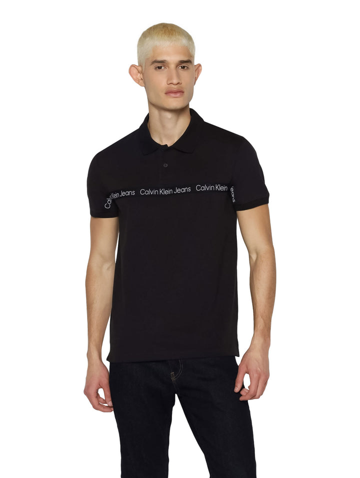 Hombre vistiendo una playera polo negra de Calvin Klein con una cinta blanca con logo en el pecho.