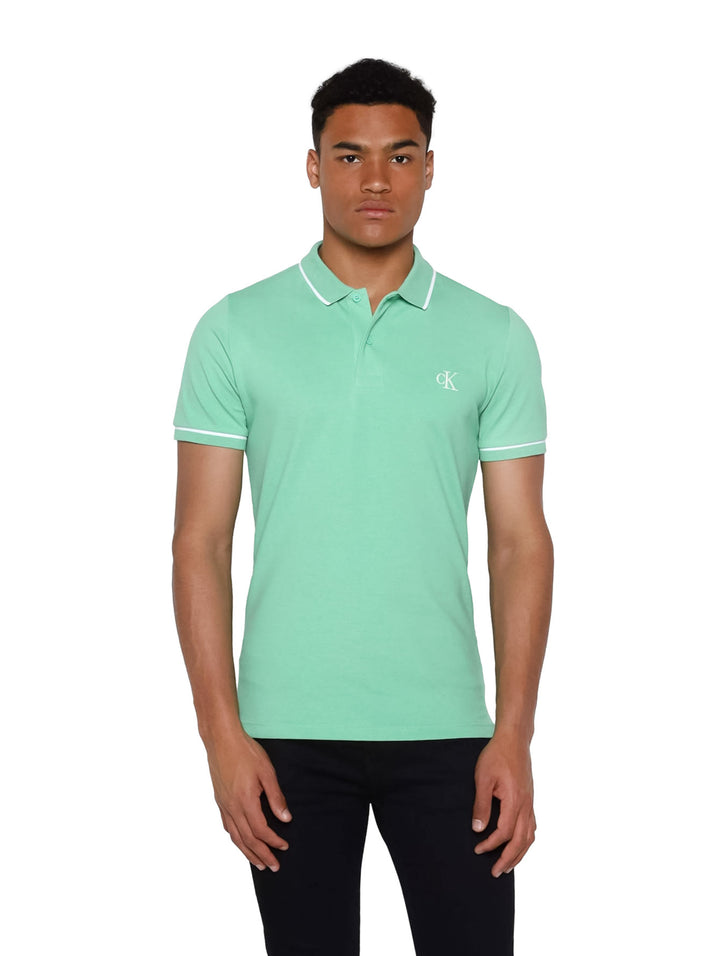 Hombre vistiendo una playera polo Calvin Klein de color verde con detalles blancos en cuello y mangas.