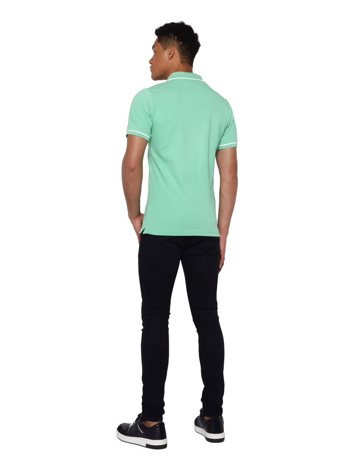 Hombre vistiendo una playera polo Calvin Klein de color verde con detalles blancos en cuello y mangas.