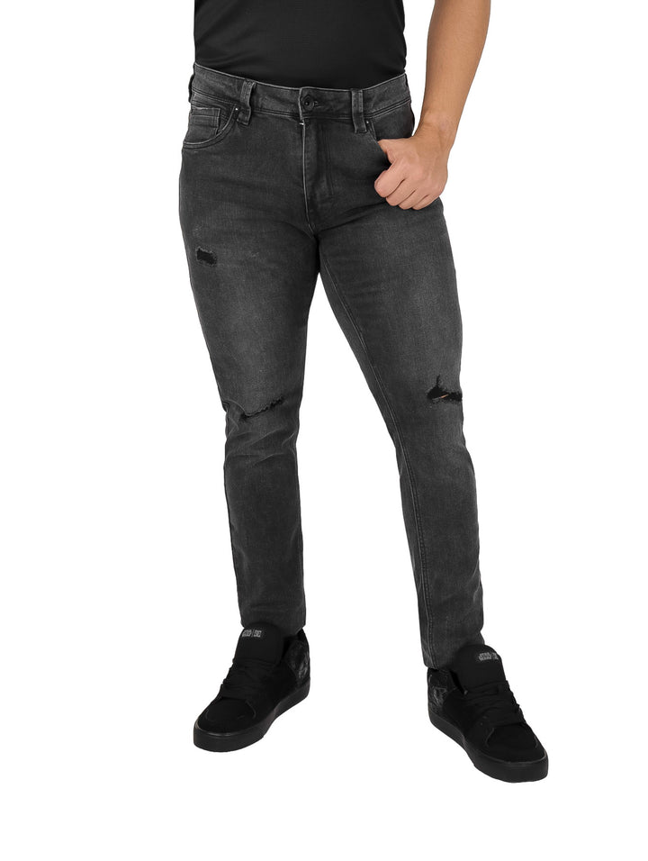Hombre vistiendo pantalones jeans negros con detalles de destrucción y calzado negro.