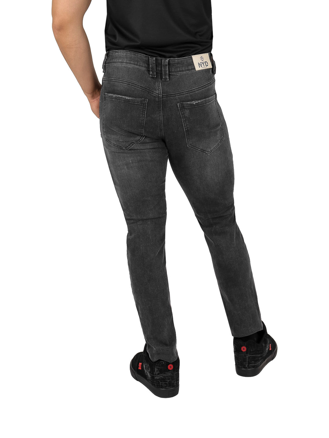 Hombre vistiendo pantalones jeans negros con detalles de destrucción y calzado negro.