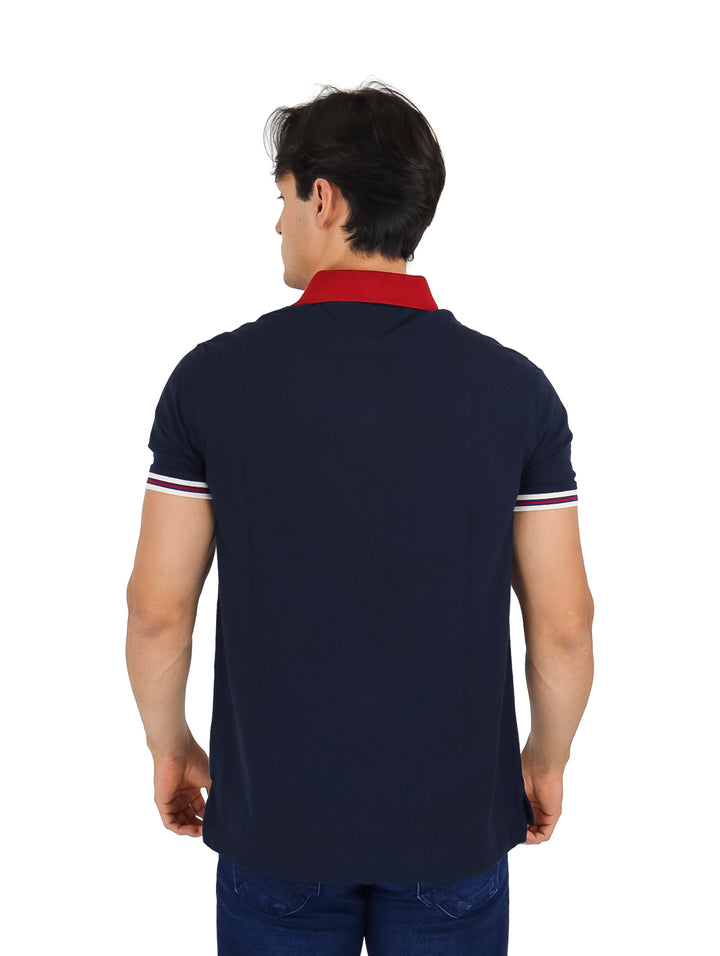 Hombre vistiendo polo Tommy Hilfiger color azul marino con cuello rojo y detalles de rayas blancas y rojas en las mangas.