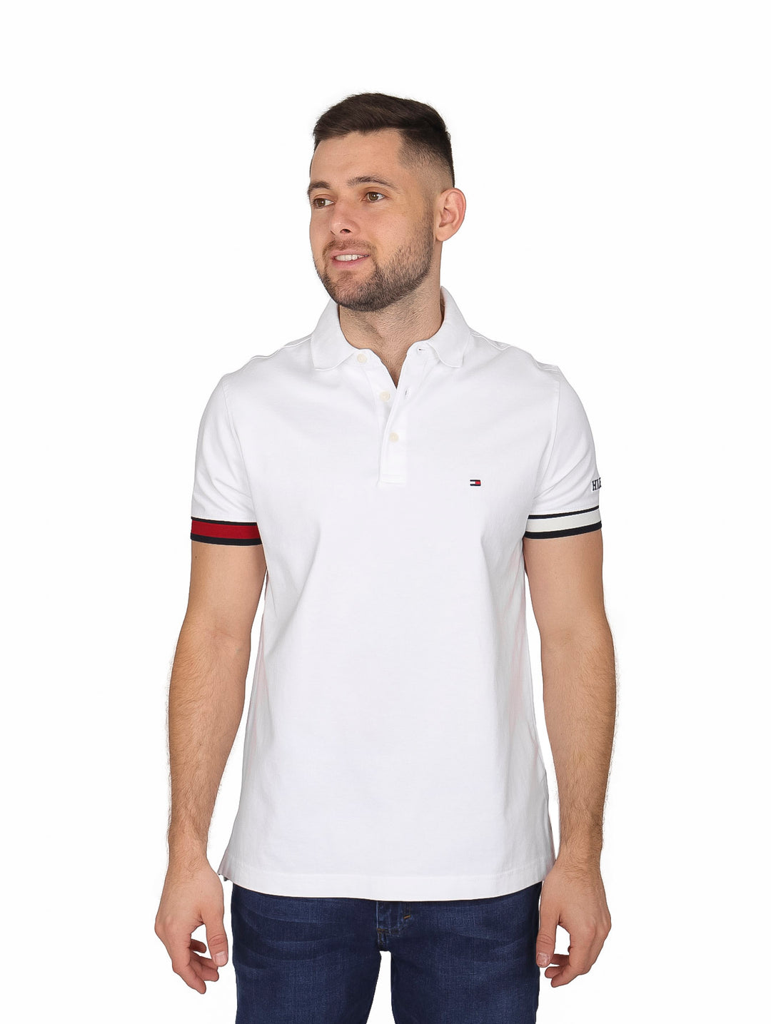 Hombre vistiendo polo blanco Tommy Hilfiger con detalles de rayas rojas y azules en las mangas.