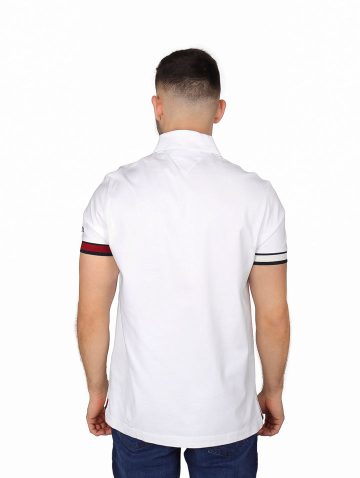 Hombre vistiendo polo blanco Tommy Hilfiger con detalles de rayas rojas y azules en las mangas.