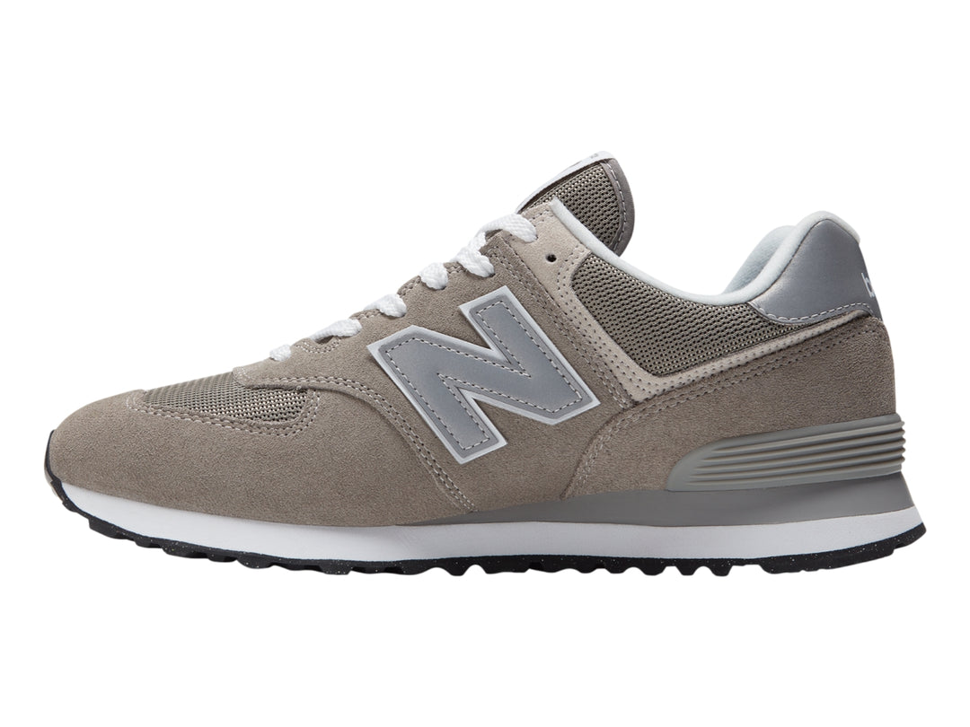 Tenis New Balance 574 color gris con suela blanca y detalles en malla.
