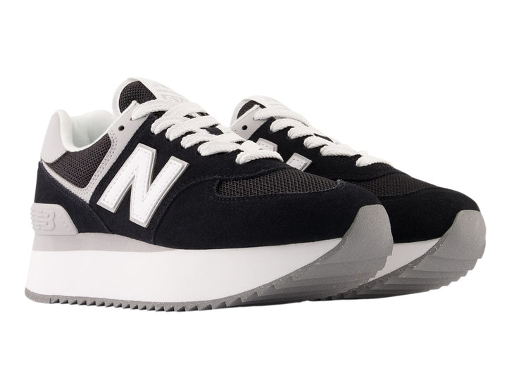 Tenis New Balance negros con suela de plataforma blanca y detalles en gris.