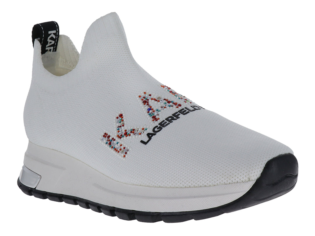 Tenis slip-on blancos de tela con suela negra y detalles de marca coloridos.