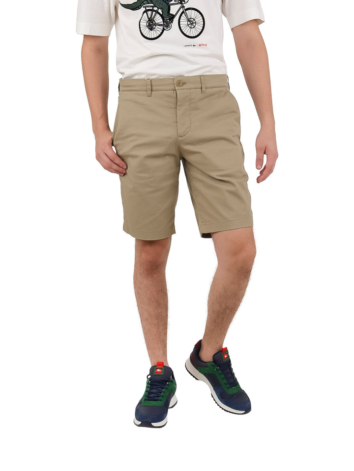 Hombre vistiendo bermudas Lacoste color beige de corte slim fit y camiseta blanca.
