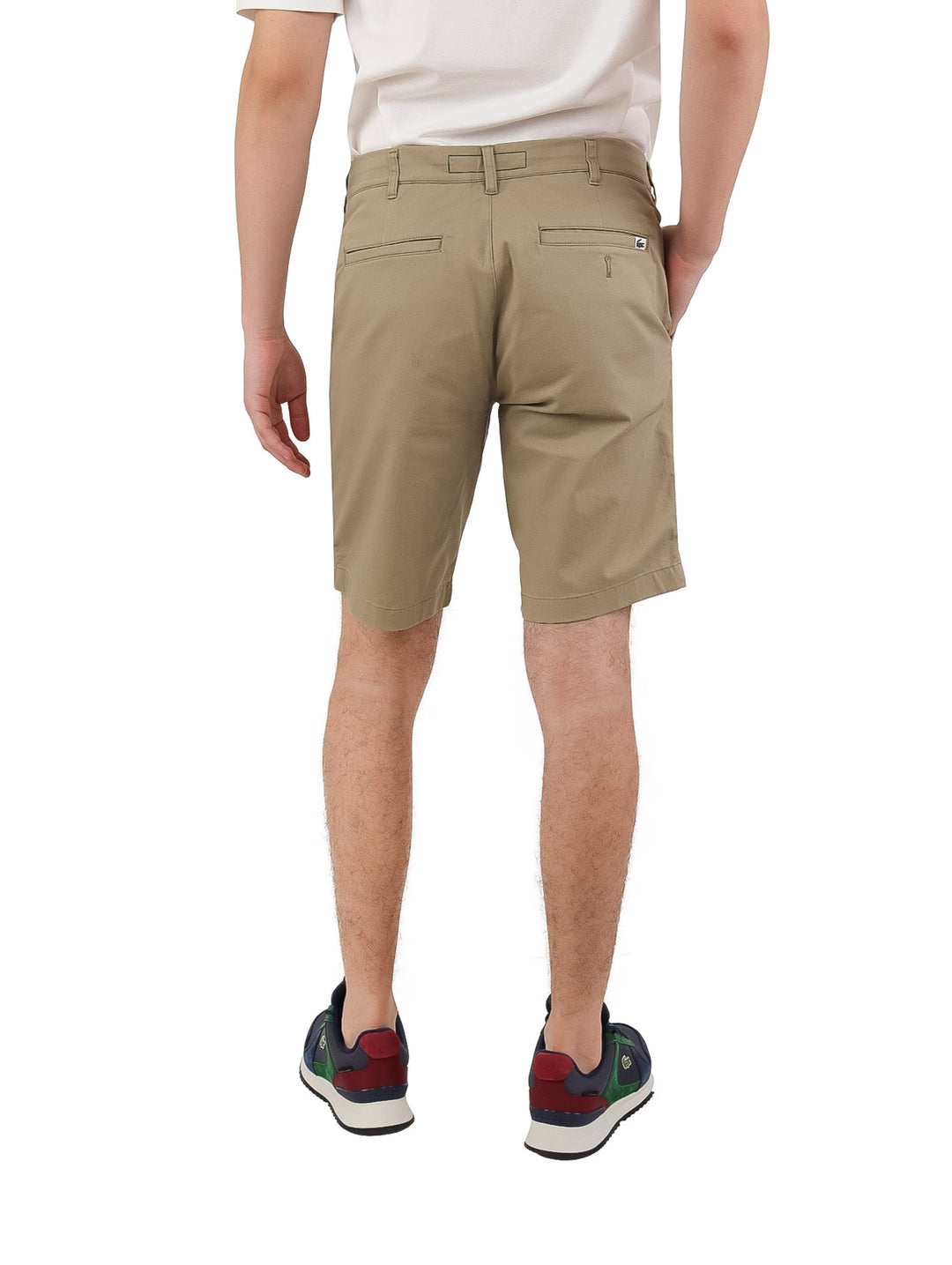 Hombre vistiendo bermudas Lacoste color beige de corte slim fit y camiseta blanca.