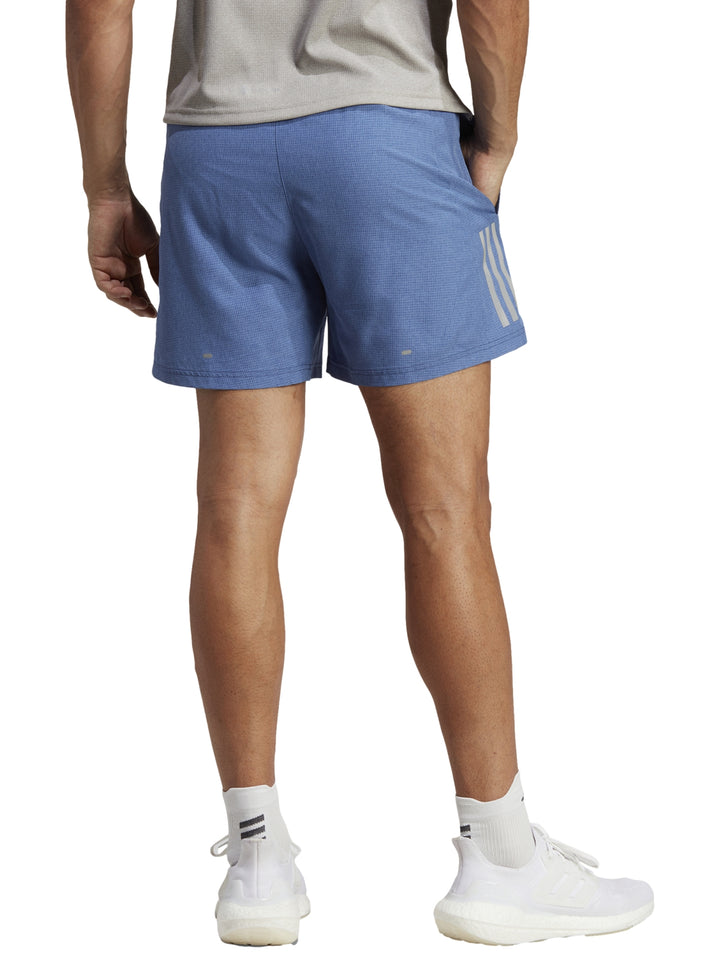 Hombre vistiendo shorts deportivos Adidas de color azul con tenis blancos.
