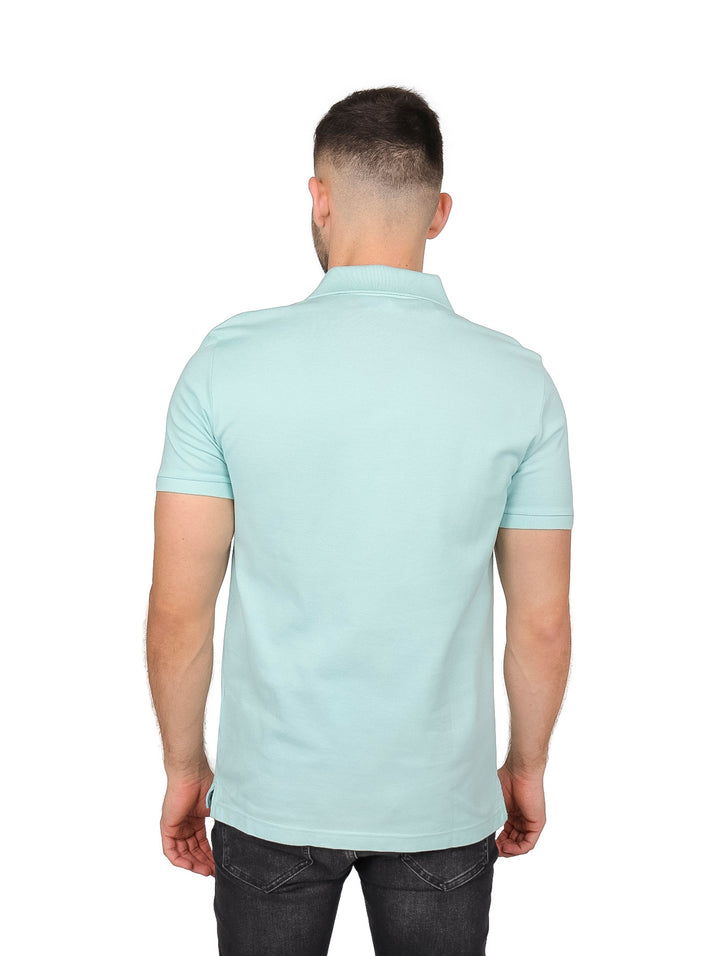 Hombre vistiendo una camiseta polo Lacoste de color verde pastel con cuello acanalado y manga corta.
