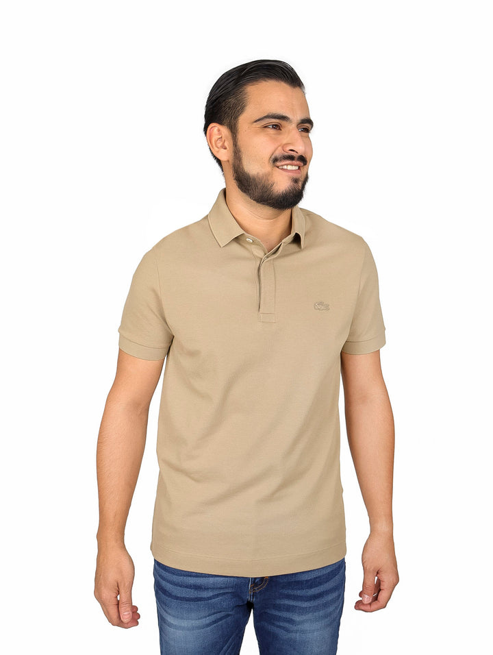Hombre vistiendo una camiseta polo Lacoste de color beige con cuello acanalado y manga corta.