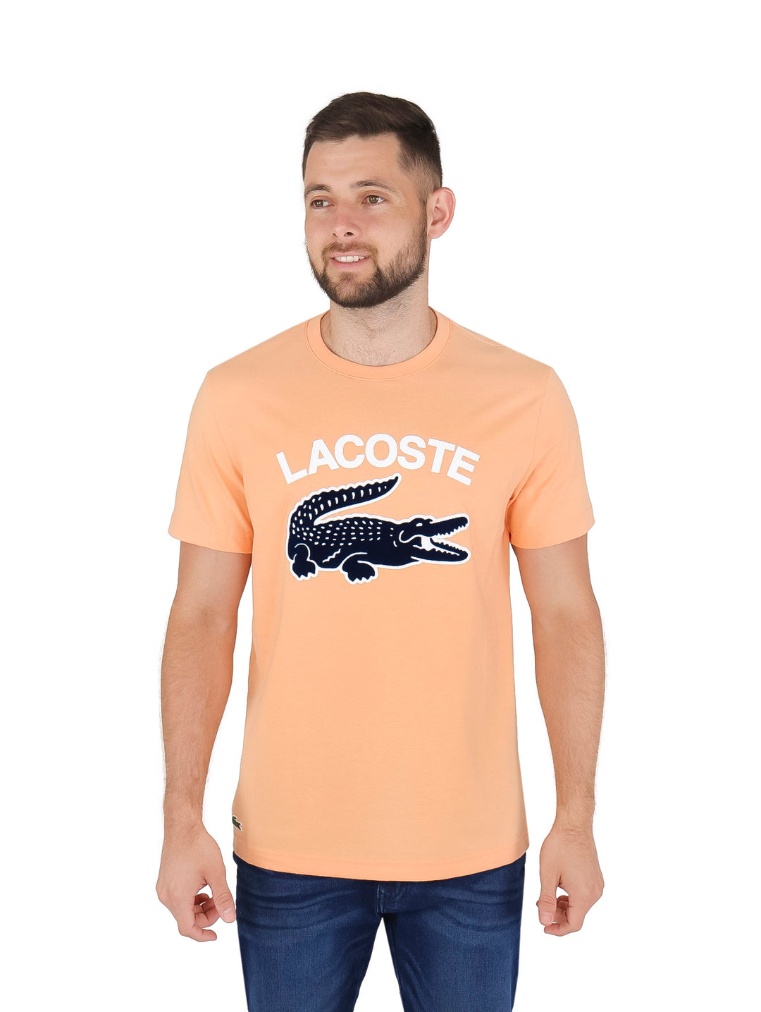 Hombre vistiendo una camiseta Lacoste color durazno con gráfico de cocodrilo y texto en el pecho.