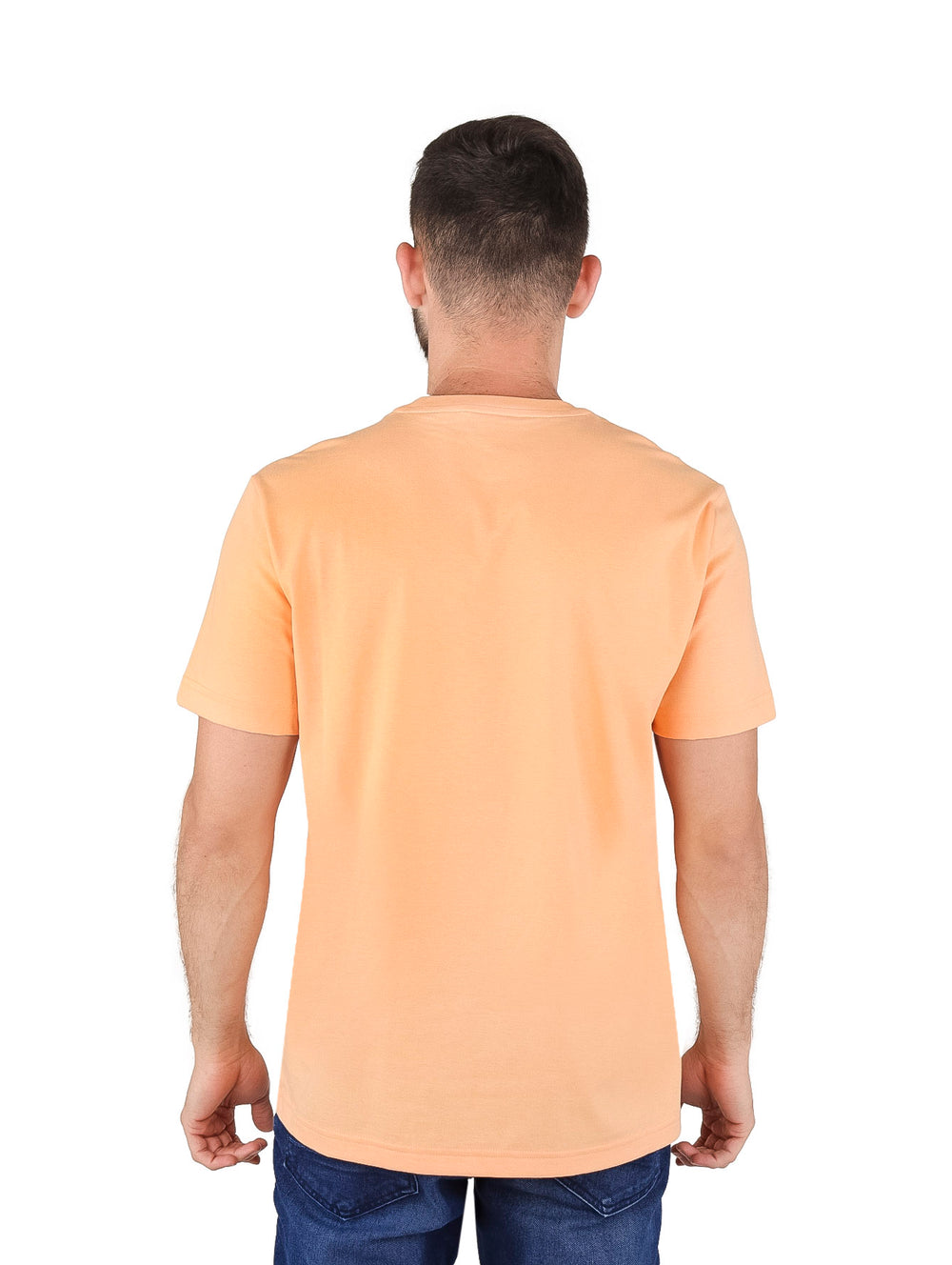 Hombre vistiendo una camiseta Lacoste color durazno con gráfico de cocodrilo y texto en el pecho.