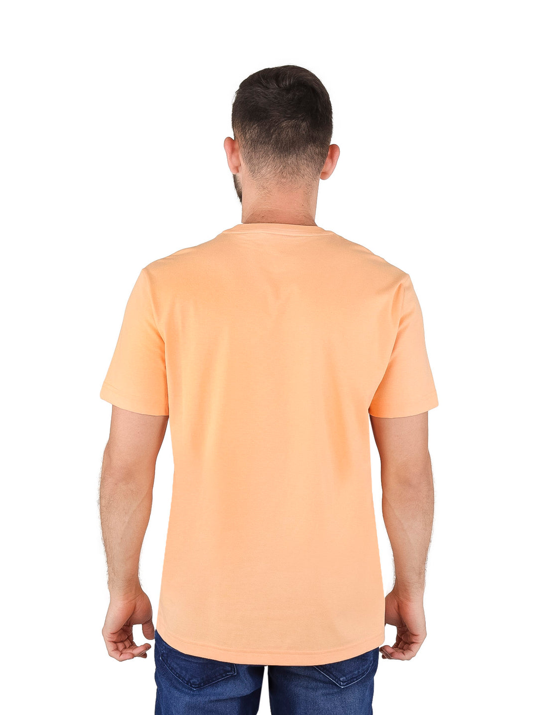 Hombre vistiendo una camiseta Lacoste color durazno con gráfico de cocodrilo y texto en el pecho.