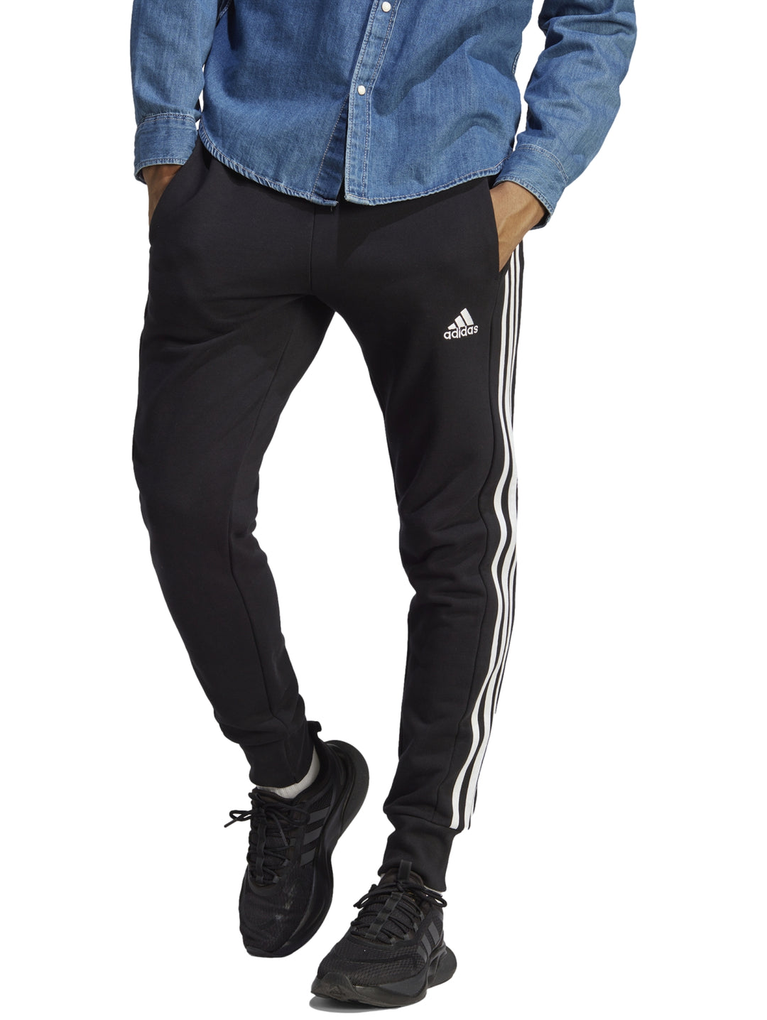 Hombre vistiendo pantalones deportivos Adidas color negro con tres franjas blancas laterales y logo en la pierna.