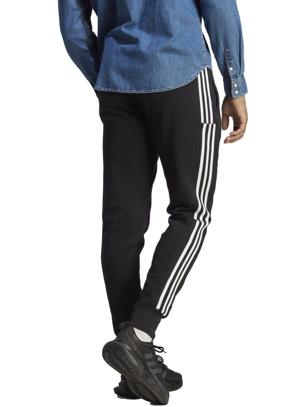 Hombre vistiendo pantalones deportivos Adidas color negro con tres franjas blancas laterales y logo en la pierna.