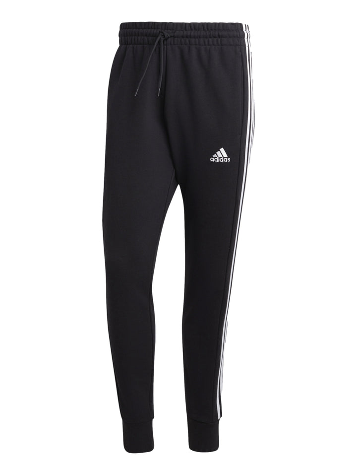 Hombre vistiendo pantalones deportivos Adidas color negro con tres franjas blancas laterales y logo en la pierna.