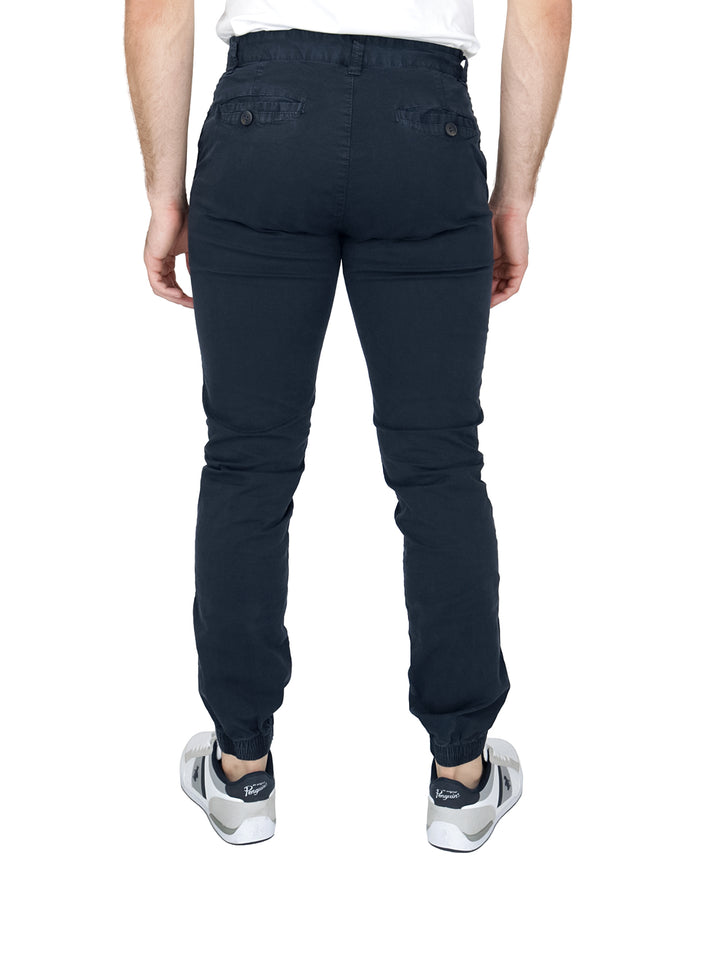 Hombre vistiendo pantalones tipo jogger color azul marino con calzado blanco sobre fondo blanco.