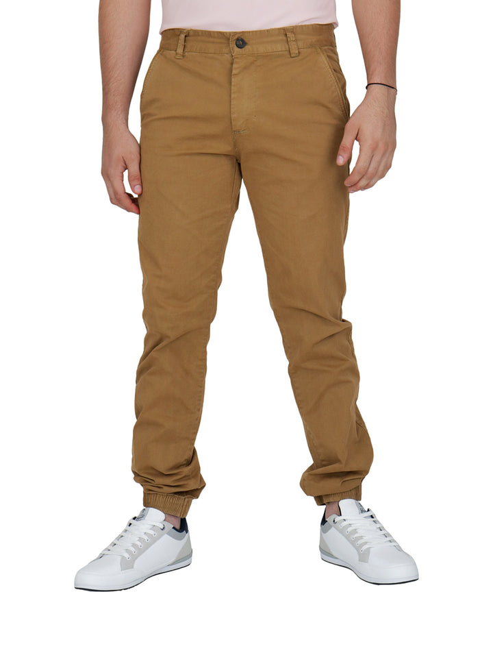 Hombre vistiendo pantalones tipo jogger color camel con calzado blanco sobre fondo blanco.