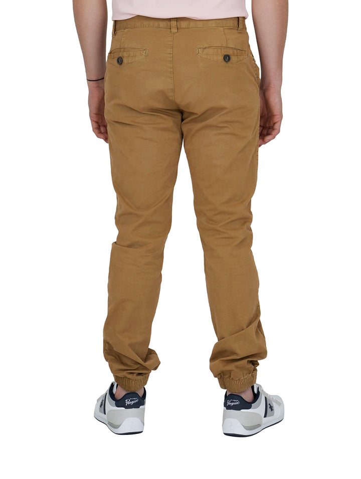Hombre vistiendo pantalones tipo jogger color camel con calzado blanco sobre fondo blanco.