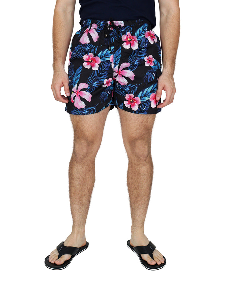 Hombre usando traje de baño corto negro con estampado de flores rosas y hojas azules.