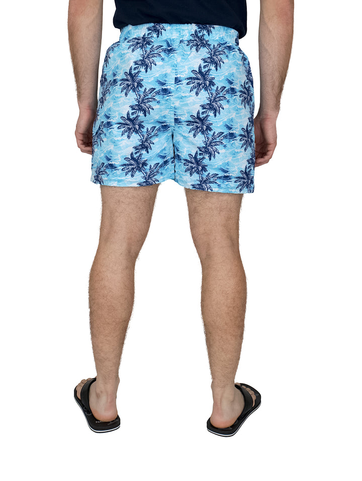 Hombre usando un traje de baño azul con estampado de palmeras y sandalias negras.
