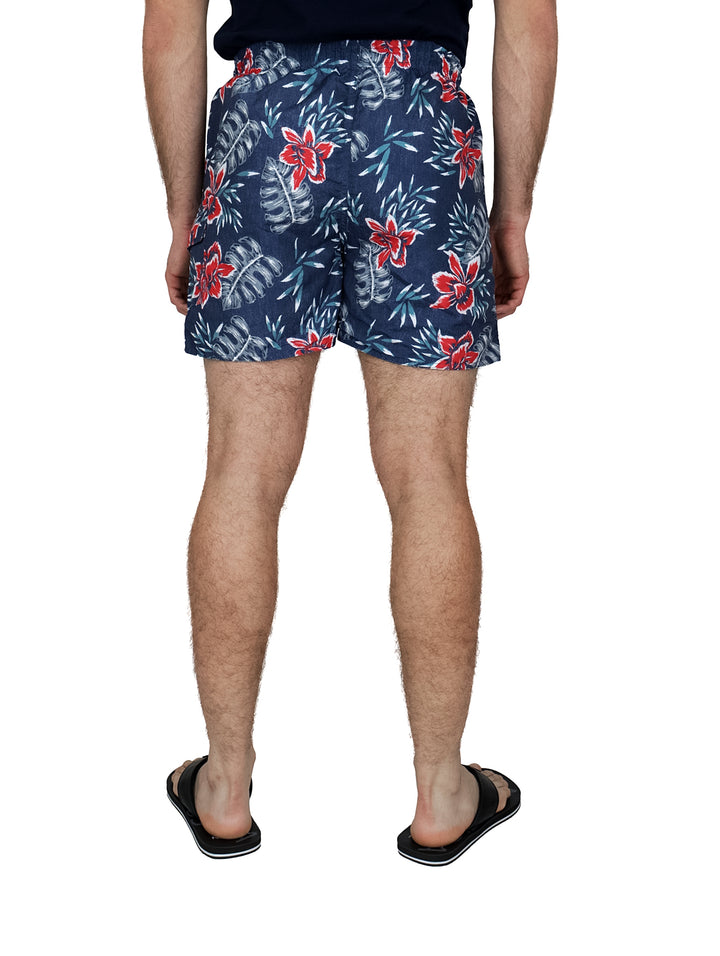 Hombre vistiendo traje de baño corto color azul marino con estampado de flores rojas y blancas.