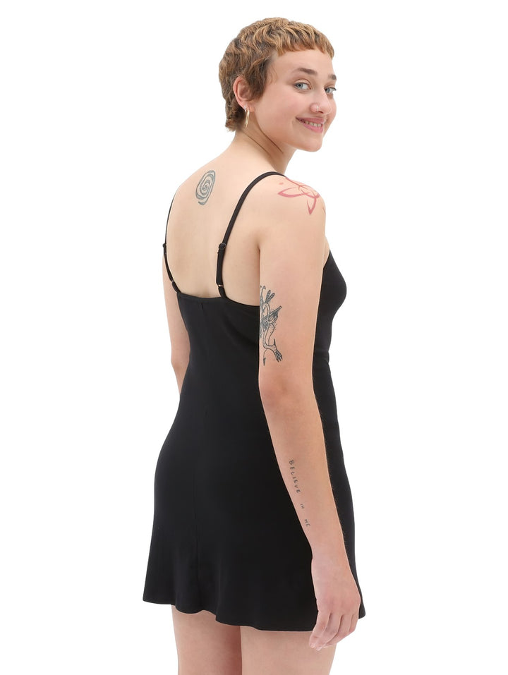 Mujer vistiendo un vestido corto negro de tirantes con el logotipo de Vans en blanco en el pecho.