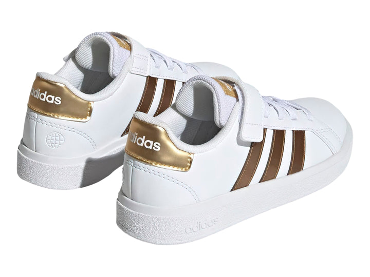 Tenis Adidas blancos con tres franjas doradas y cierre de velcro.