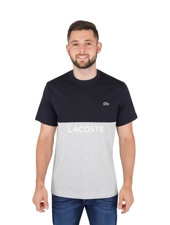 Hombre vistiendo camiseta Lacoste de dos tonos en azul marino y gris con logotipo frontal.
