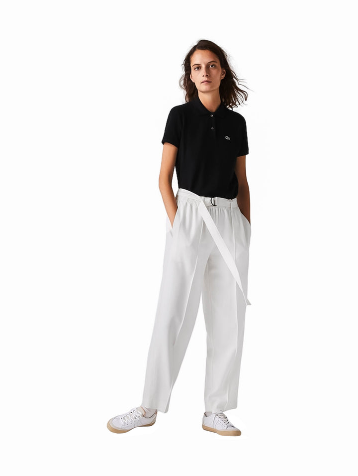Mujer vistiendo una playera polo Lacoste de color negro, pantalones blancos y tenis blancos.