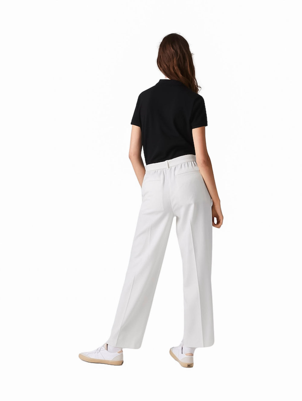 Mujer vistiendo una playera polo Lacoste de color negro, pantalones blancos y tenis blancos.
