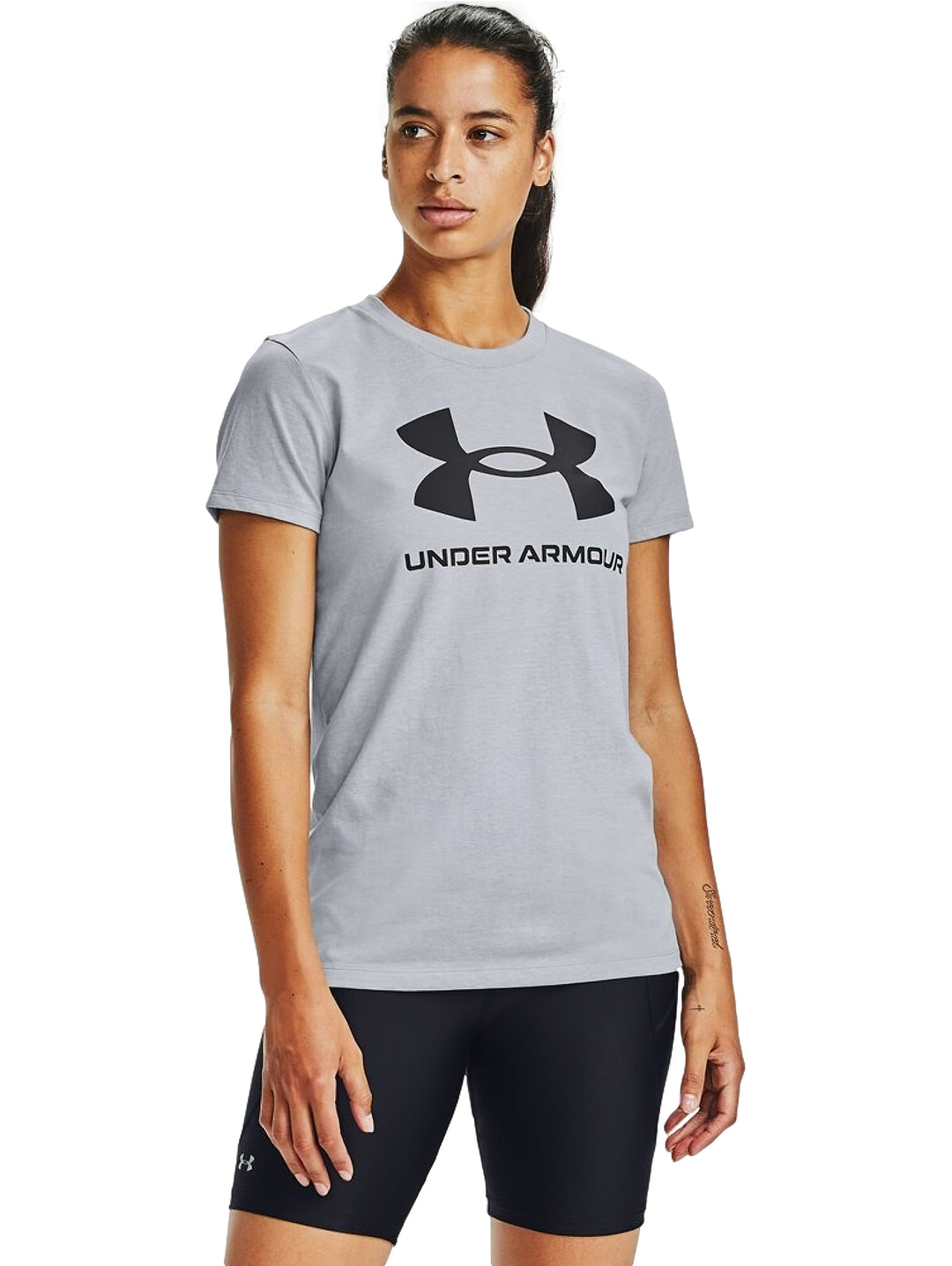 Mujer vistiendo playera Under Armour de color gris con logotipo negro en el pecho y shorts deportivos negros.