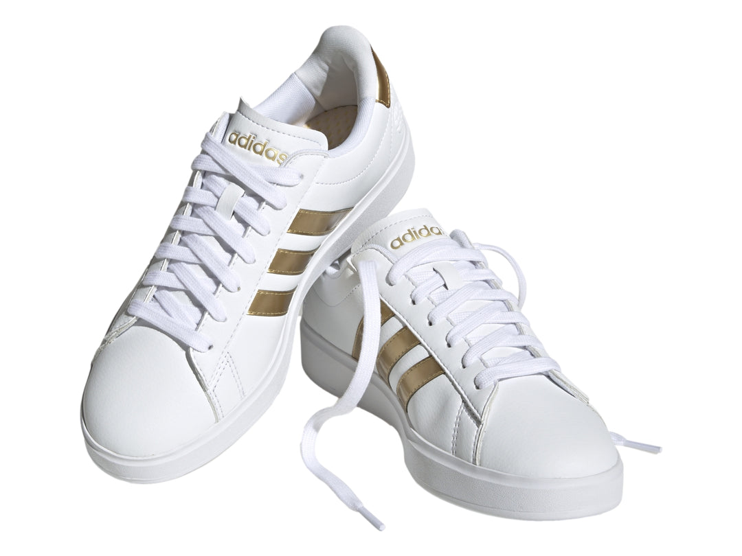Tenis Adidas Grand Court color blanco con tres franjas laterales y detalle en el talón en color dorado.