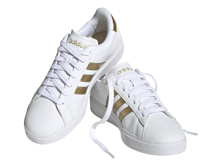 Tenis Adidas Grand Court color blanco con tres franjas laterales y detalle en el talón en color dorado.