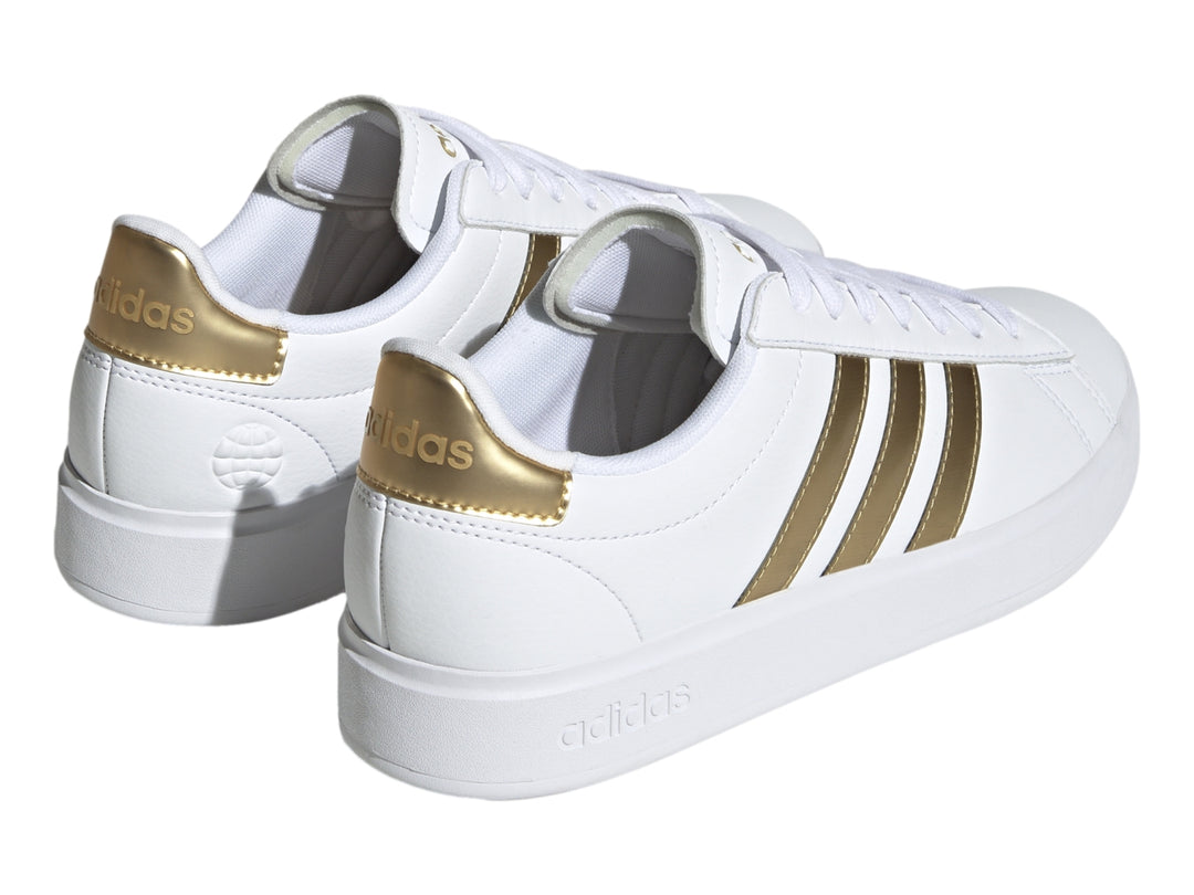 Tenis Adidas Grand Court color blanco con tres franjas laterales y detalle en el talón en color dorado.