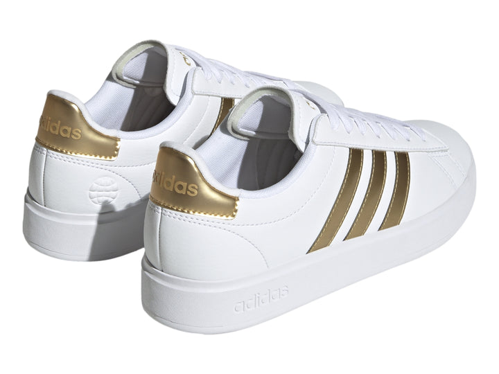 Tenis Adidas Grand Court color blanco con tres franjas laterales y detalle en el talón en color dorado.